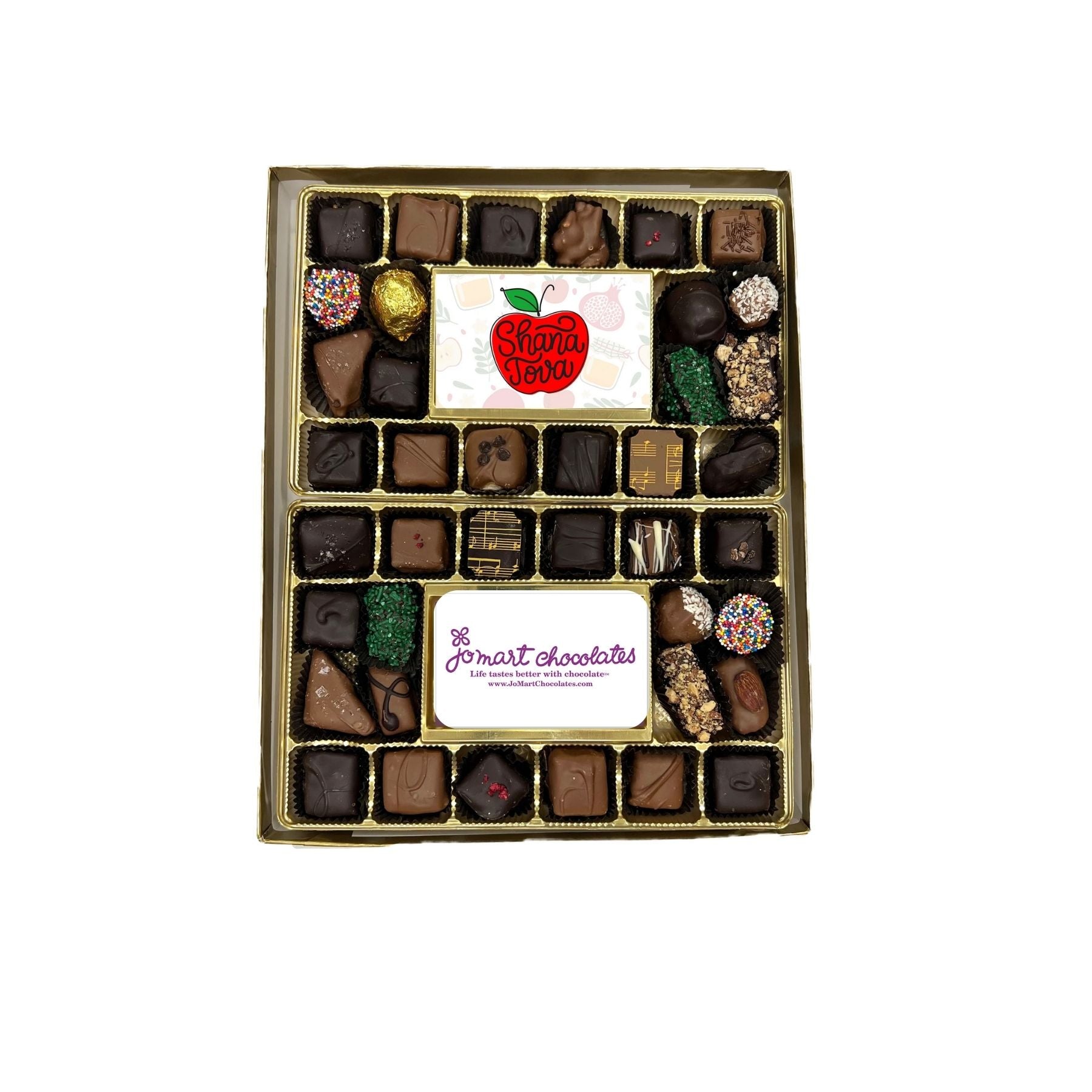 A boxed assortment of chocolates and truffles displayed in a gold-lidded rectangular box on a plain white background. Two white labels are visible inside the box, one with a red apple logo reading 'Shana Tova' and another with purple script reading 'JoMart Chocolates'.