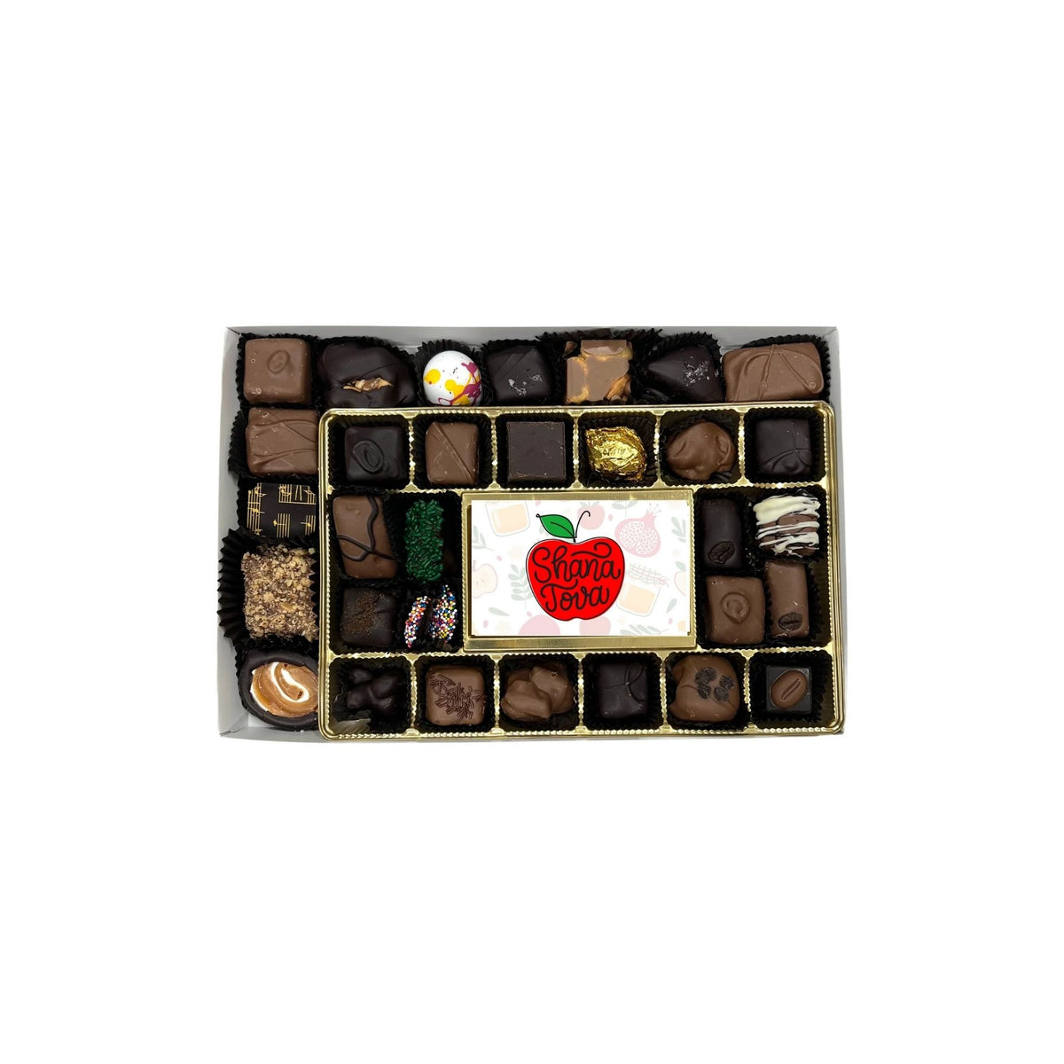An assortment of gourmet chocolates in an open gift box with a central label that reads 'Shana Tova' with a red apple logo, set against a plain white background.