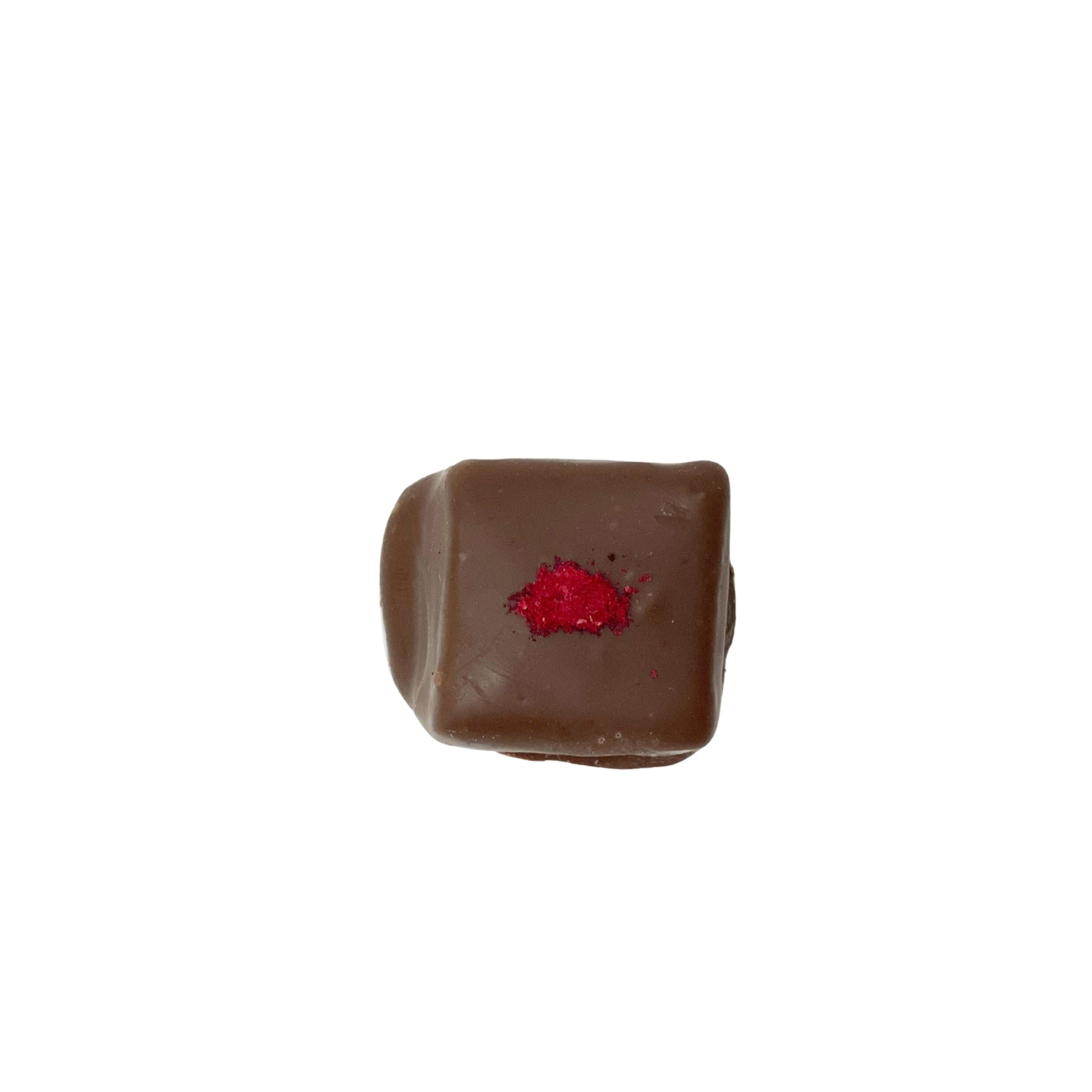 A single square piece of dark chocolate with a small pile of red powder on top, isolated on a solid white background.