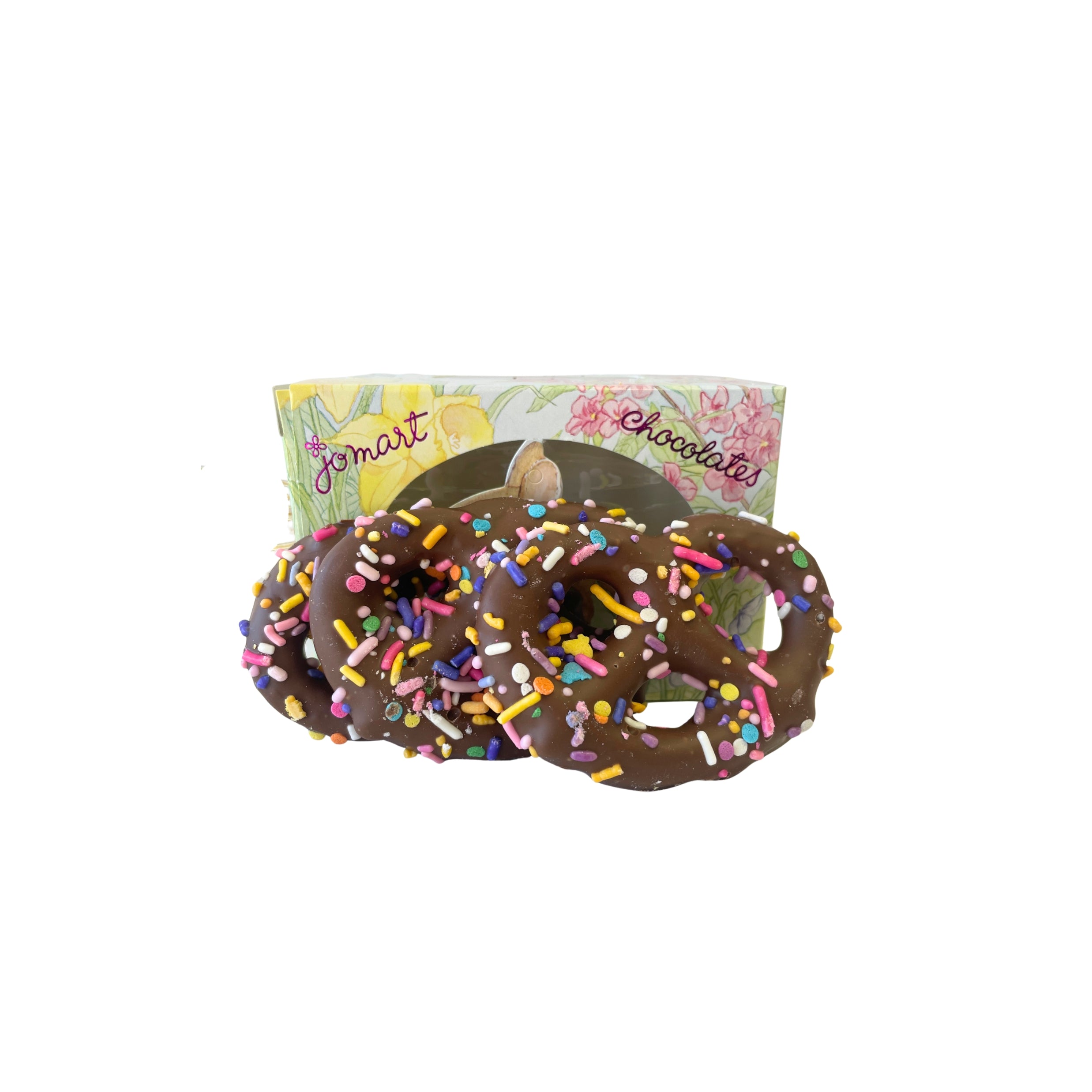 Chocolate pretzels with sprinkles in front of a floral-patterned box on a white background
